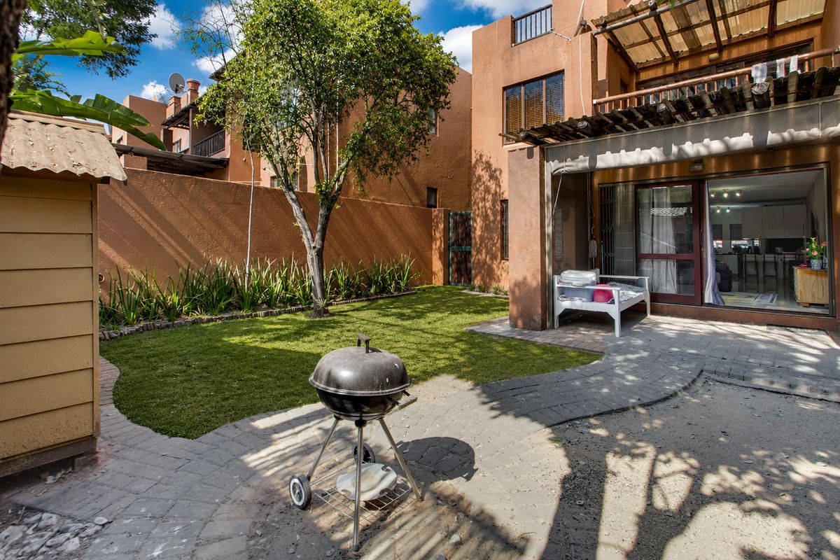 Rear garden area featuring a paved patio, lawn, and timber pergola structure attached to the apartment building.