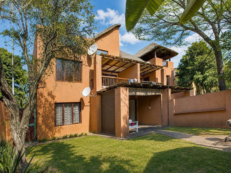 Rear view of a multi-story apartment building featuring a thatched roof, timber pergolas, private balcony, patio area, and a small garden.