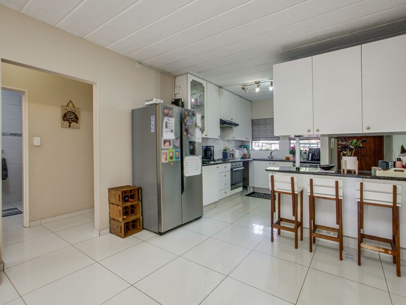 A functional kitchen featuring white cabinetry, granite countertops, a breakfast bar, and tiled flooring, with an adjacent doorway leading to a bathroom area.