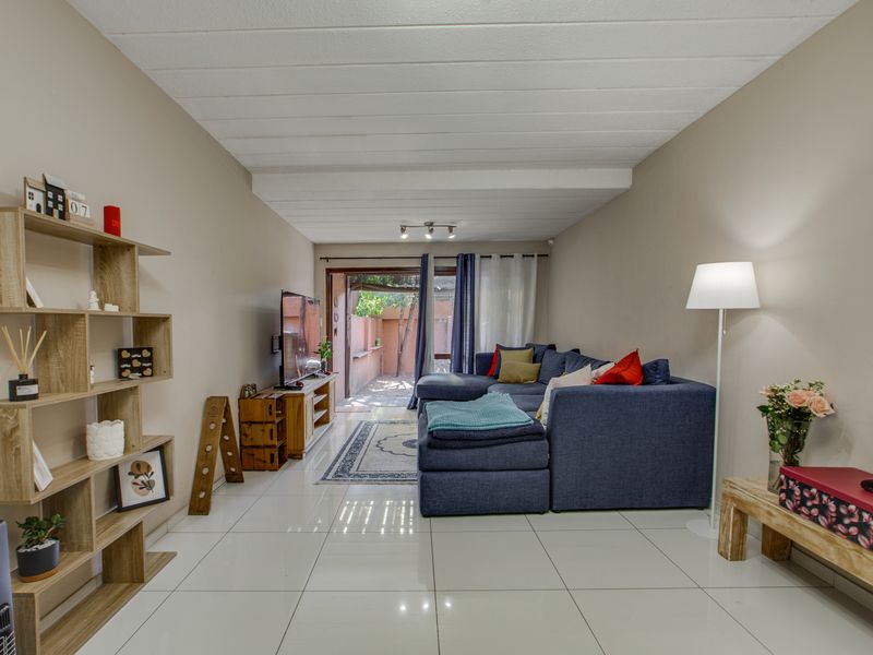 A well-lit living room featuring polished tile flooring, an exposed beam ceiling, and a sliding glass door providing access to the outdoor area.