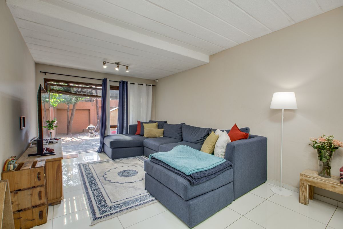A bright living room featuring tiled flooring, track lighting, and a sliding glass door providing direct access to the outdoor patio area.