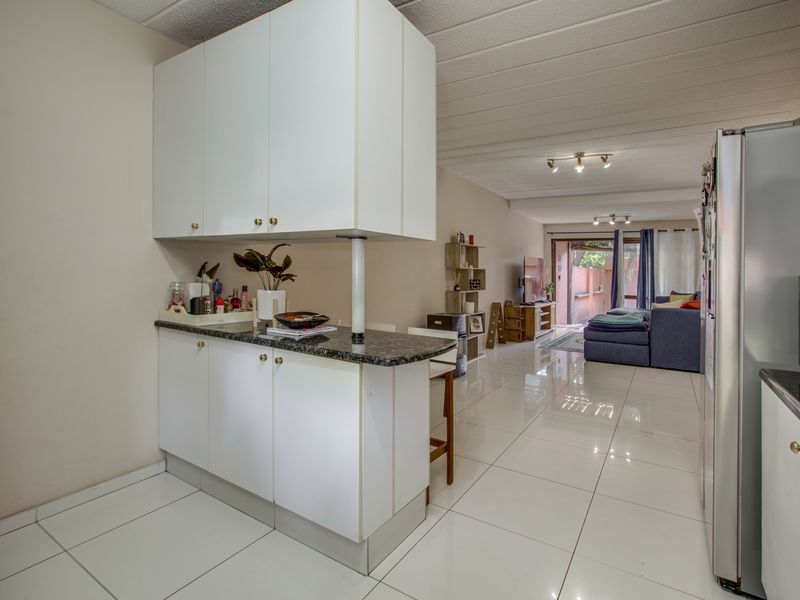 Open plan living area featuring a kitchen with white cabinetry, granite breakfast bar, and polished tiled flooring leading to a rear patio.