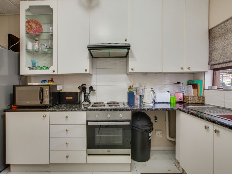 A functional kitchen featuring white cabinetry, granite countertops, a built-in oven, electric hob, and a tiled backsplash with an integrated sink.