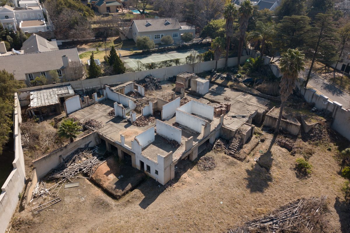 Aerial view of a residential plot featuring a demolished structure, concrete slab foundation, and perimeter walling in a suburban neighborhood setting.