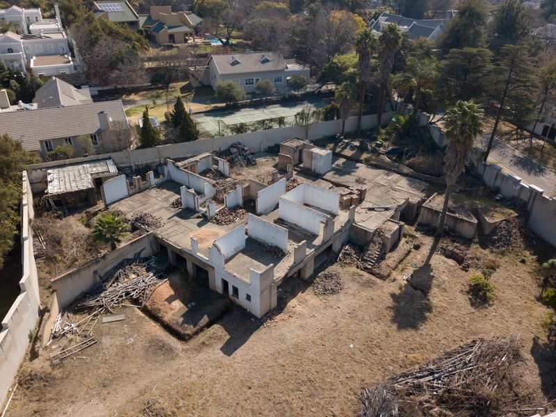 Aerial view of a residential plot featuring a demolished structure, concrete slab foundation, and perimeter walling in a suburban neighborhood setting.