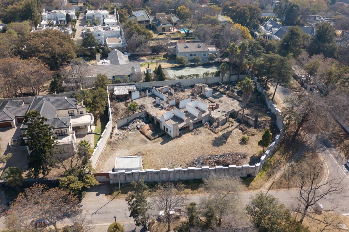 Aerial view of a residential plot featuring a partially demolished structure, concrete slab foundation, and perimeter walling in a suburban neighborhood.