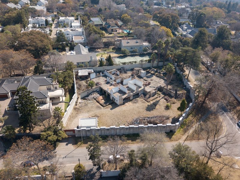 Aerial view of a residential plot featuring a partially demolished structure, concrete slab foundation, and perimeter walling in a suburban neighborhood.