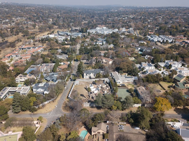 Aerial view of a vacant residential plot featuring a dilapidated structure, situated within an established suburban neighborhood with mature trees and street access.
