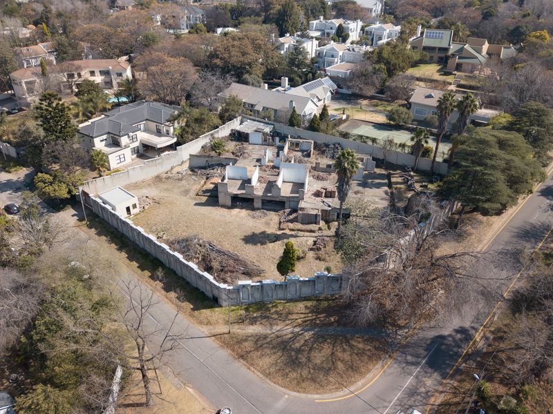 Aerial view of a vacant residential plot featuring a perimeter wall and the concrete foundation of a partially demolished structure.