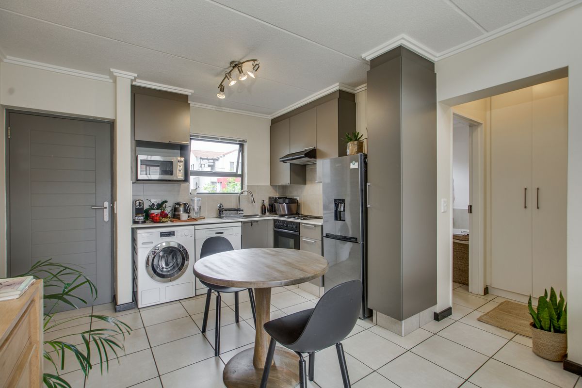 A compact, modern kitchen featuring sleek grey cabinetry, tiled flooring, integrated laundry plumbing, and built-in cooking appliances, offering a functional and efficient workspace.