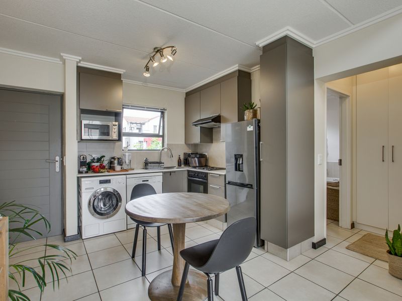 A compact, modern kitchen featuring sleek grey cabinetry, tiled flooring, integrated laundry plumbing, and built-in cooking appliances, offering a functional and efficient workspace.