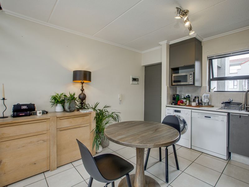 Open-plan kitchen and dining area featuring modern cabinetry, integrated microwave, tiled flooring, and functional spotlight lighting in a well-maintained apartment setting.