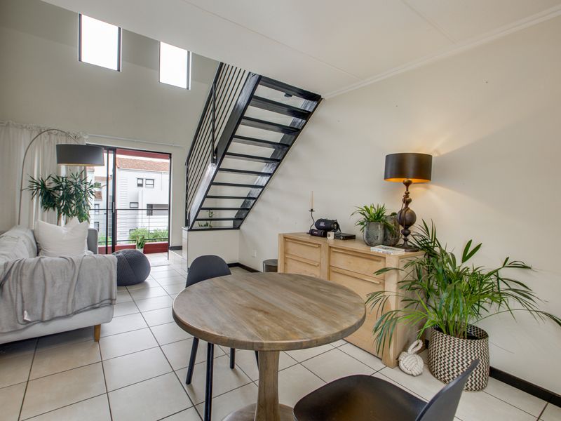 Bright open-plan living area featuring high ceilings, tiled floors, a modern metal staircase, and a sliding door leading to a balcony.