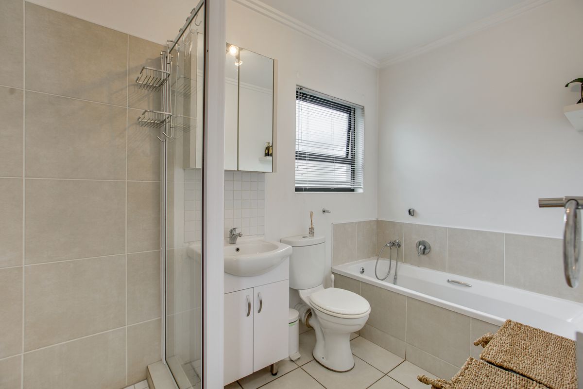 A clean, well-maintained bathroom featuring a separate shower enclosure, bathtub, vanity unit with mirrored cabinet, and neutral wall and floor tiling.
