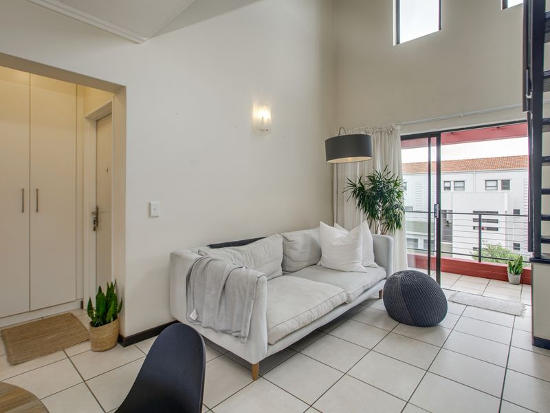 A bright living room featuring high ceilings, tiled flooring, built-in storage, and a sliding door providing access to a balcony.