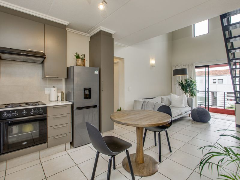 Open-plan living area featuring a modern kitchen with built-in appliances, tiled flooring, and a staircase leading to an upper level with double volume ceilings.