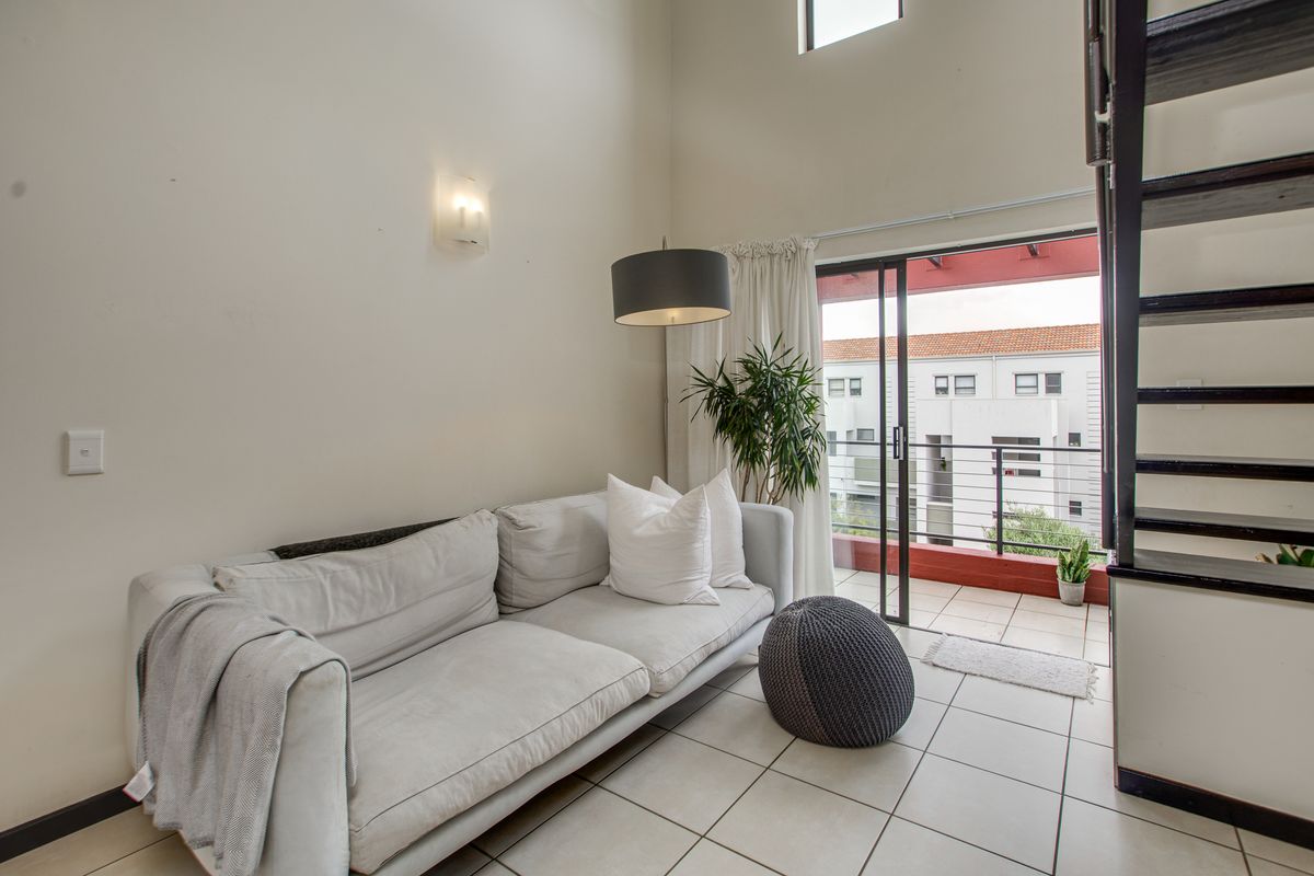 Bright living area with high ceilings, tiled flooring, and direct access to a balcony through sliding glass doors.