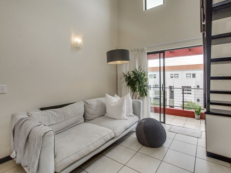 Bright living area with high ceilings, tiled flooring, and direct access to a balcony through sliding glass doors.