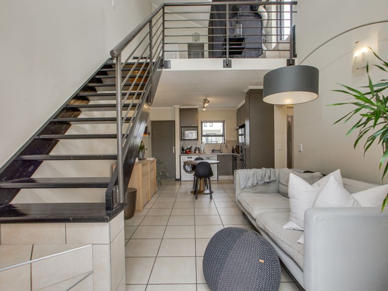 Open-plan living area featuring a modern metal staircase leading to a mezzanine level, with an integrated kitchen and tiled flooring throughout.
