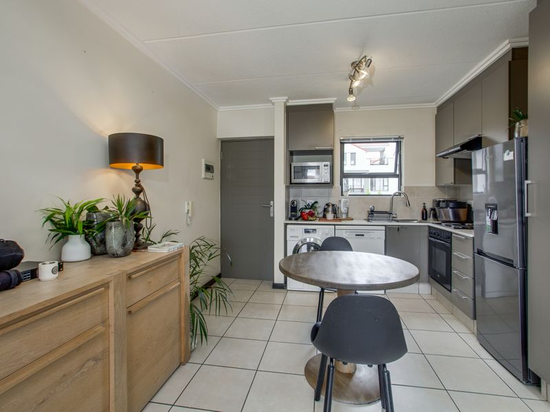 An open-plan kitchen and dining area featuring modern grey cabinetry, tiled flooring, and integrated appliances, creating a functional and cohesive living space.