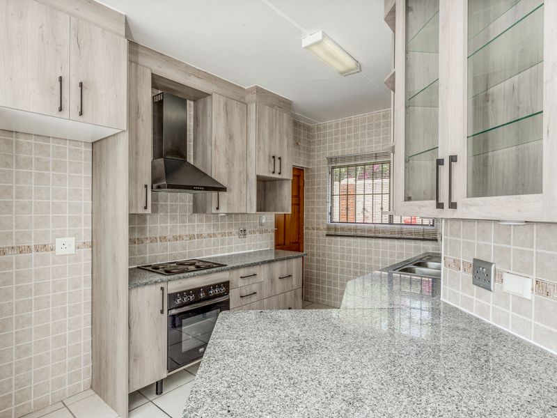 A clean, modern kitchen featuring light wood-grain cabinetry, granite countertops, a built-in oven, electric hob, and a tiled backsplash.