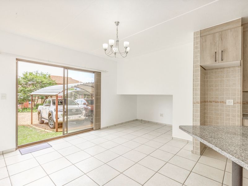 Bright open-plan living and kitchen area featuring tiled flooring, a granite breakfast bar, and sliding glass doors leading to the exterior.
