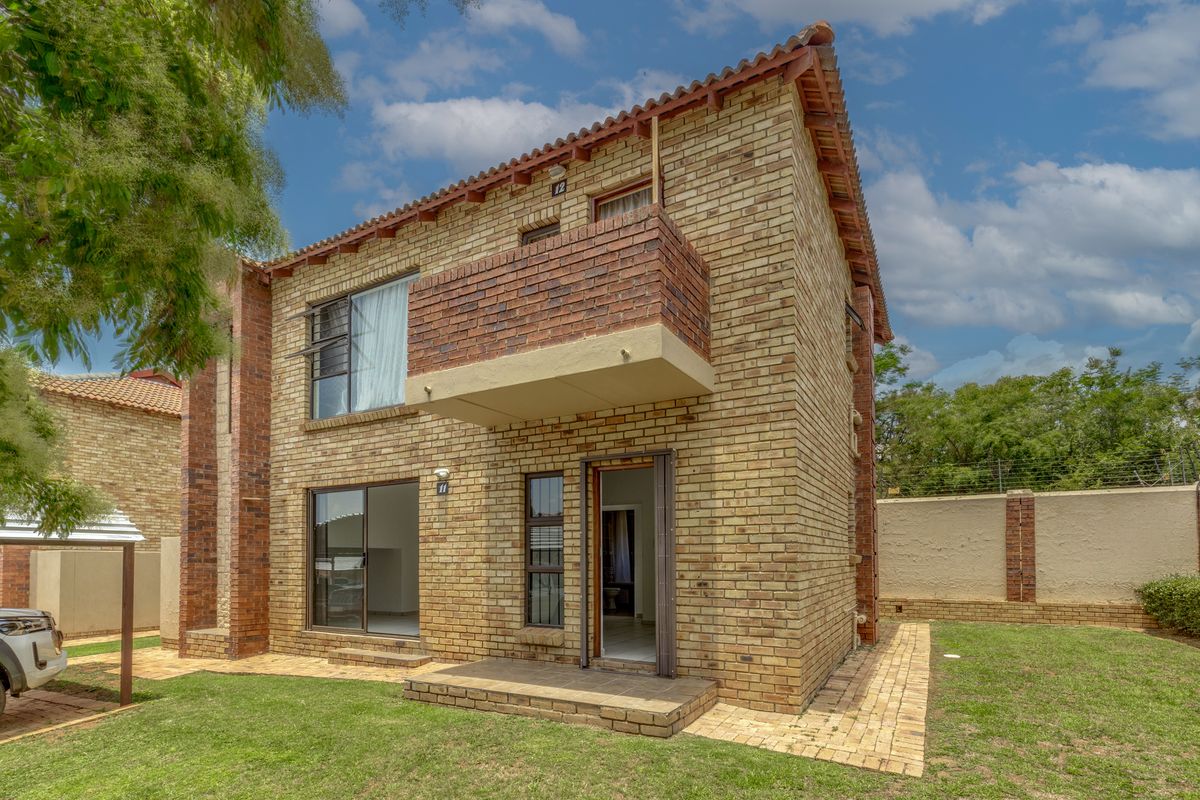 Rear view of a double-story face brick townhouse featuring a private balcony, paved patio area, and enclosed garden with perimeter security fencing.