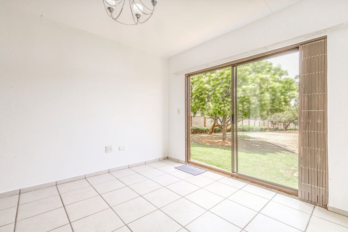 A bright, empty living room featuring neutral tiled flooring and a large sliding glass door providing direct access to the garden.