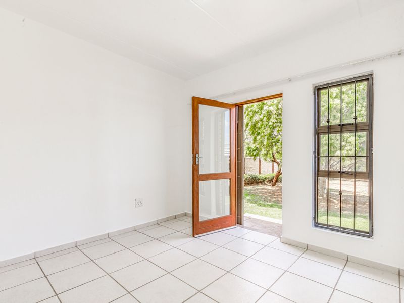 A bright, empty bedroom featuring tiled flooring, a built-in cupboard, and direct access to the garden through a timber door with security gate.