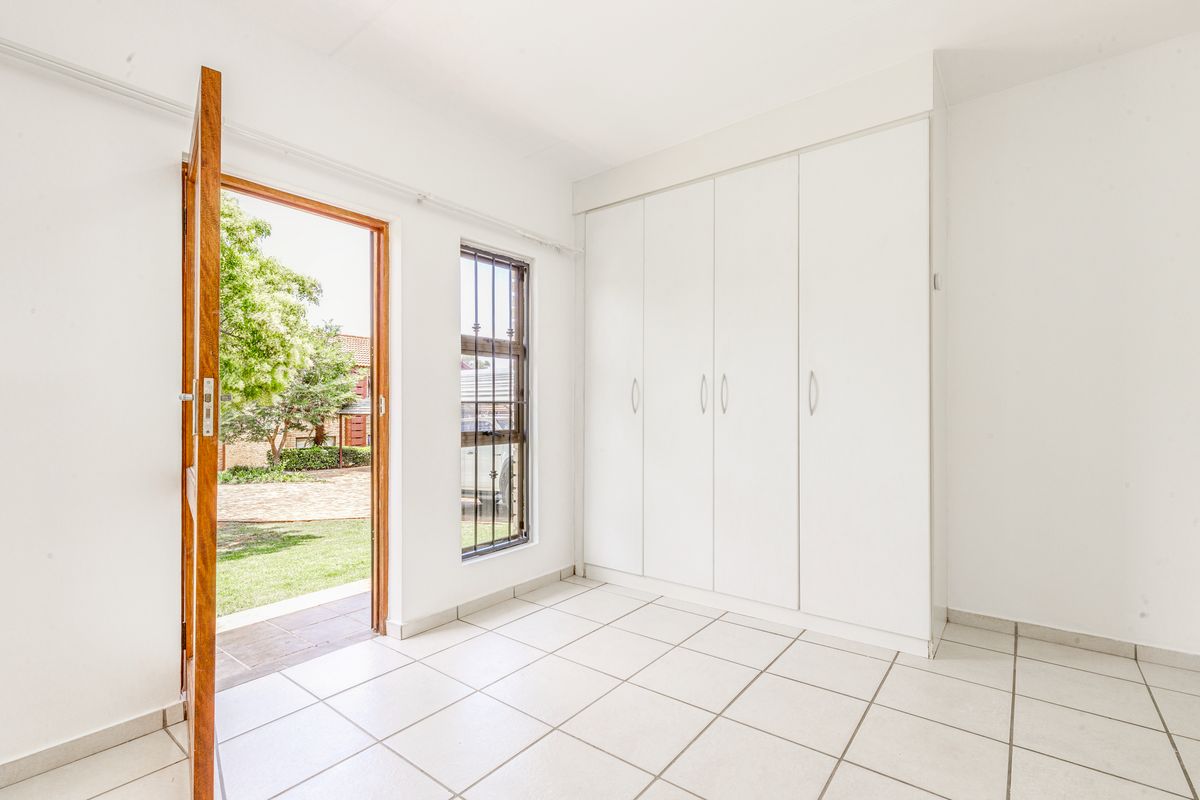 A bright, empty bedroom featuring white built-in cupboards, tiled flooring, and direct access to the garden through an external door.