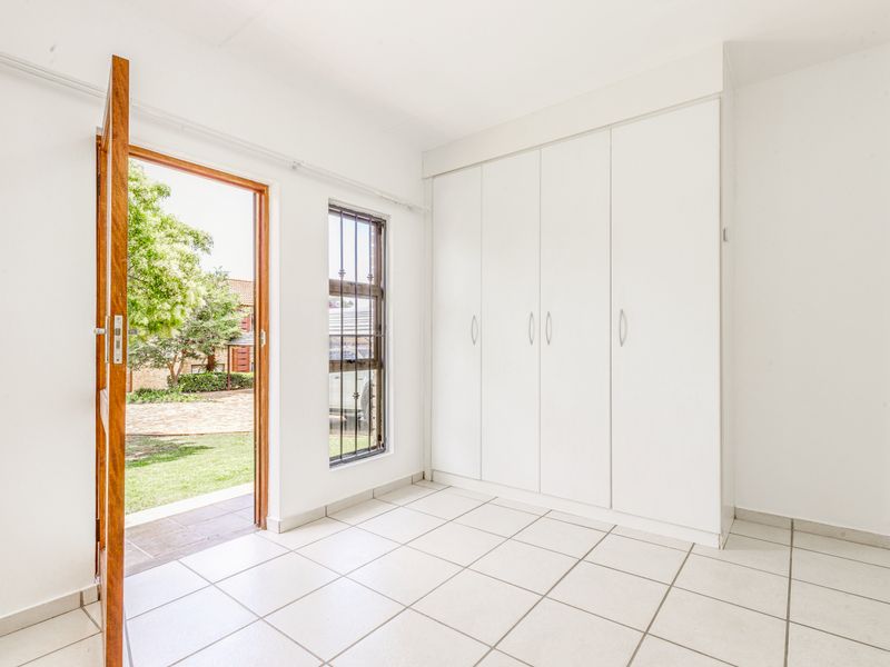 A bright, empty bedroom featuring white built-in cupboards, tiled flooring, and direct access to the garden through an external door.
