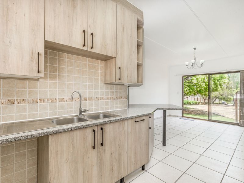 Open plan kitchen featuring light wood cabinetry, granite countertops, and a breakfast bar, flowing into a bright living area with sliding door access to the garden.