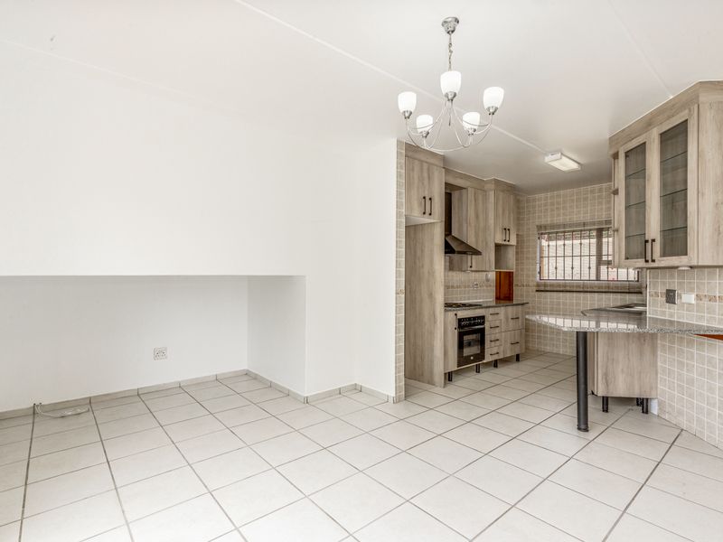 Open-plan kitchen and dining area featuring light wood-look cabinetry, granite countertops, built-in oven, extractor fan, and neutral tiled flooring throughout.