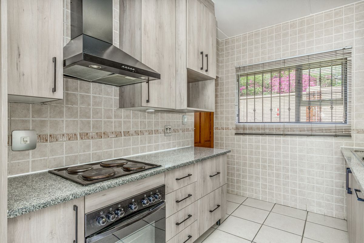 A functional kitchen featuring light wood-grain cabinetry, granite countertops, a built-in electric oven and hob, and neutral tiled finishes throughout.