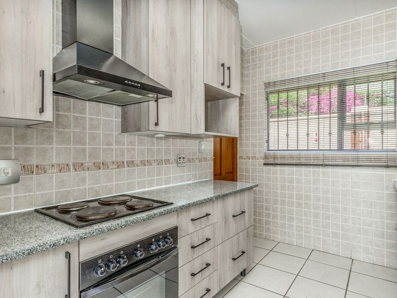 A functional kitchen featuring light wood-grain cabinetry, granite countertops, a built-in electric oven and hob, and neutral tiled finishes throughout.