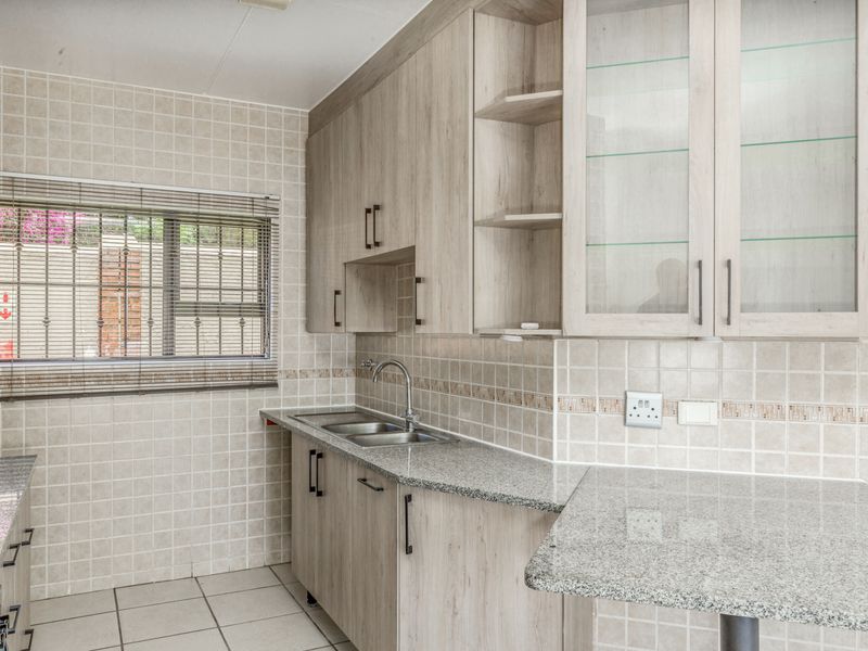 A functional kitchen featuring light wood-look cabinetry, granite countertops, a double basin sink, and neutral tiled finishes.