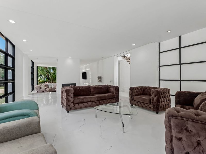 Spacious, modern living area featuring polished marble flooring, recessed lighting, and large black-framed windows that provide ample natural light and garden views.