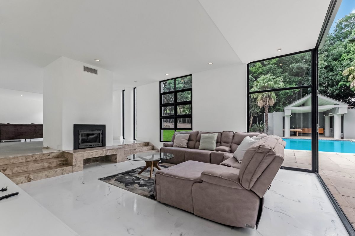 Spacious modern living room featuring a built-in fireplace, marble-look flooring, and expansive floor-to-ceiling windows with direct access to the pool area.