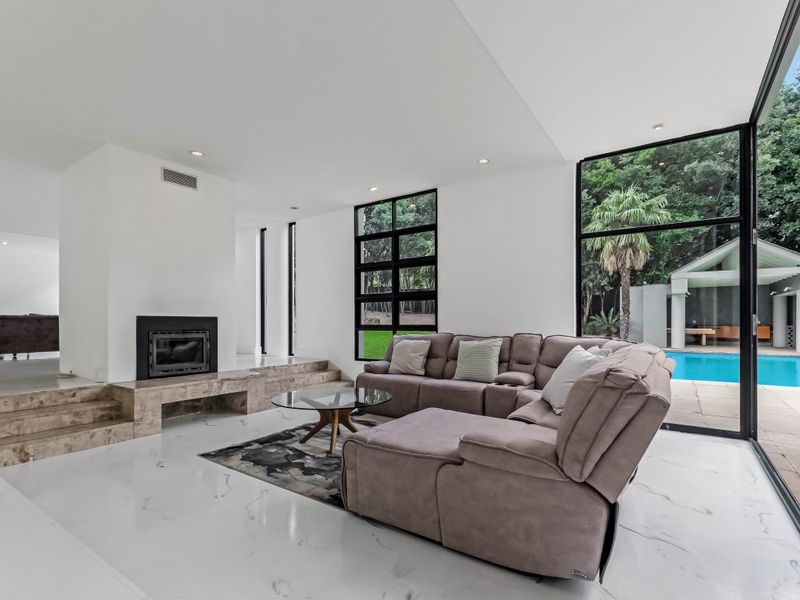 Spacious modern living room featuring a built-in fireplace, marble-look flooring, and expansive floor-to-ceiling windows with direct access to the pool area.