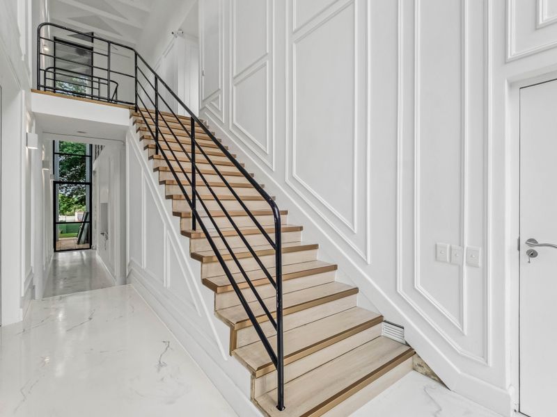 Elegant entrance hallway featuring a grand staircase with timber treads, wrought iron balustrade, sophisticated wainscoting, and polished marble flooring.