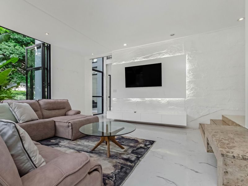 Modern living room featuring marble flooring, a textured stone feature wall with integrated lighting, and large bi-fold doors opening to the garden.