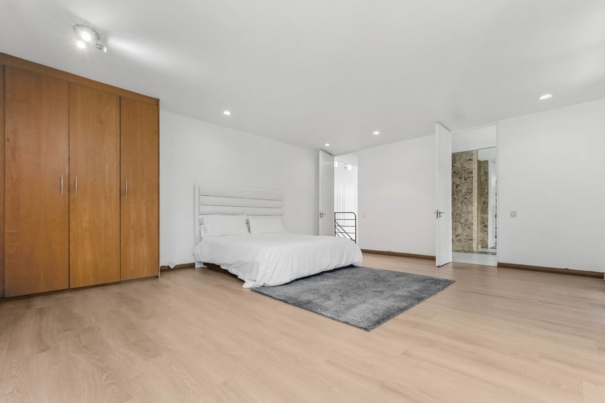 Spacious bedroom featuring light laminate flooring, built-in wooden wardrobe, recessed lighting, and direct access to an adjoining bathroom area.