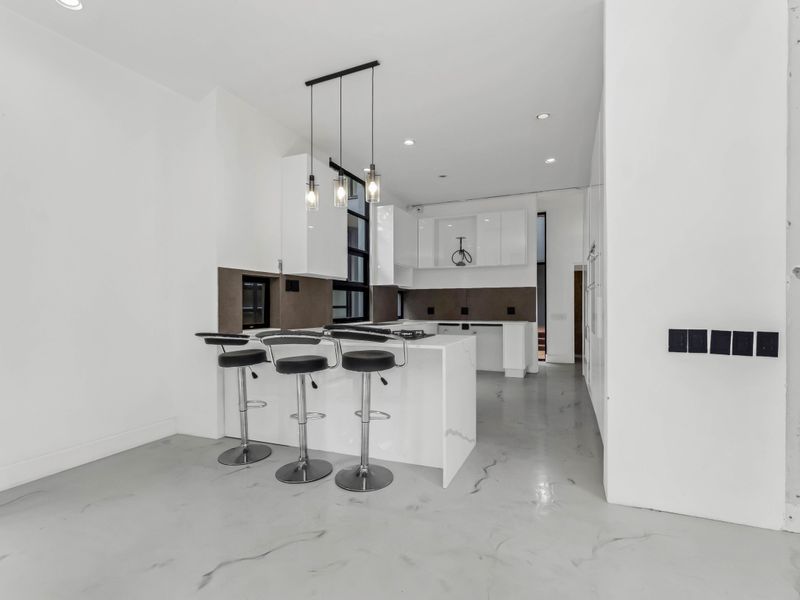 Modern kitchen featuring a central island with stone countertops, sleek white cabinetry, and contemporary pendant lighting in an open-plan layout.