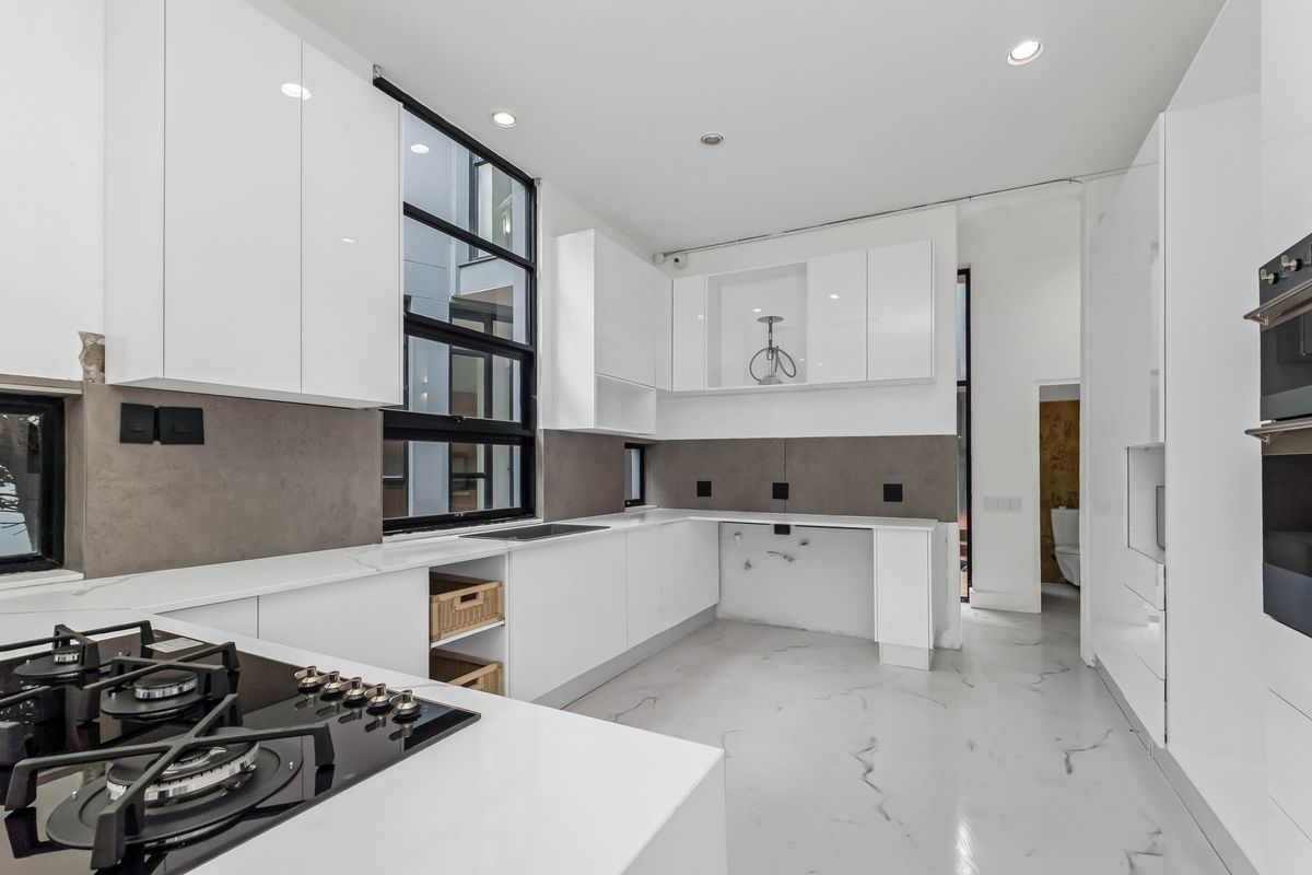 Modern kitchen featuring white cabinetry, stone countertops, a gas hob, and built-in oven, with a clean, minimalist aesthetic and marble-look flooring.