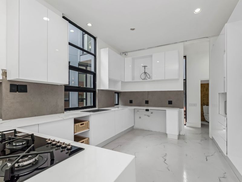 Modern kitchen featuring white cabinetry, stone countertops, a gas hob, and built-in oven, with a clean, minimalist aesthetic and marble-look flooring.