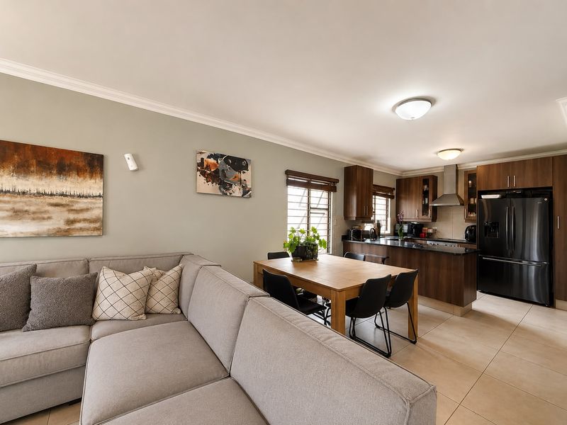Open-plan living and kitchen area featuring tiled floors, modern wood-finish cabinetry, stone countertops, and a stainless steel extractor fan.