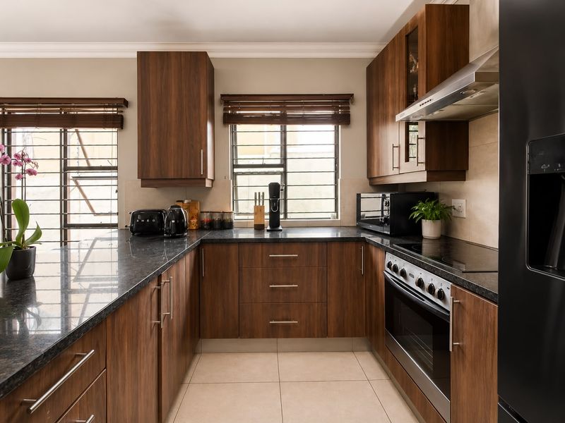 A well-maintained kitchen featuring dark wood cabinetry, granite countertops, integrated oven and hob, and tiled flooring with natural light from windows.