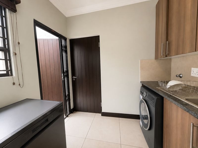 A functional laundry room featuring built-in cabinetry, stone countertops, a stainless steel sink, and direct access to the exterior via a security gate.
