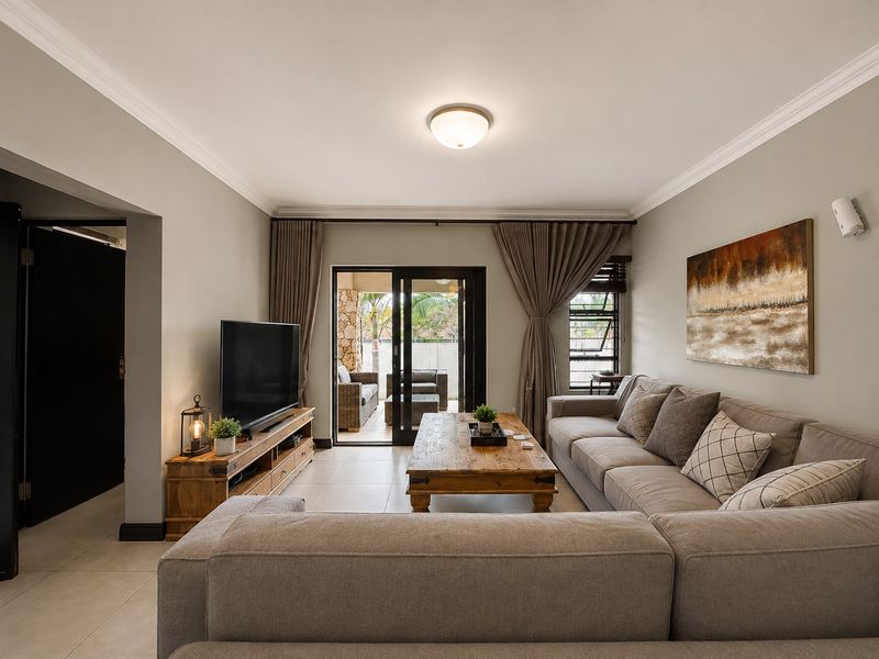 A well-maintained living room featuring neutral tiled flooring, cove cornicing, and large sliding glass doors that provide seamless access to the outdoor patio area.