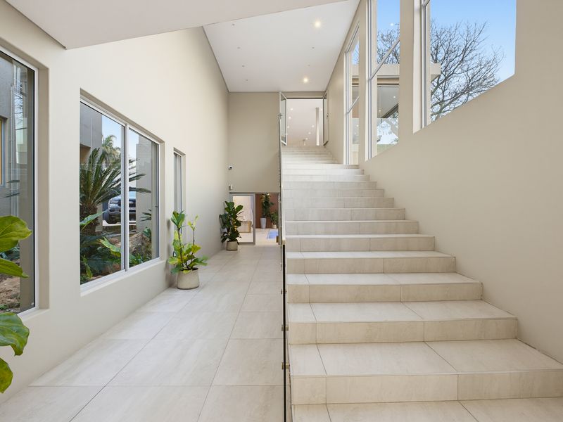 Spacious modern entrance hall featuring a grand tiled staircase with a glass balustrade, high ceilings, and large windows providing ample natural light.